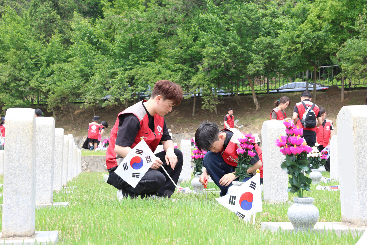 롯데건설 '샤롯데 봉사단'이 묘비 옆에 태극기를 꽂고 있다. [사진=롯데건설 제공]